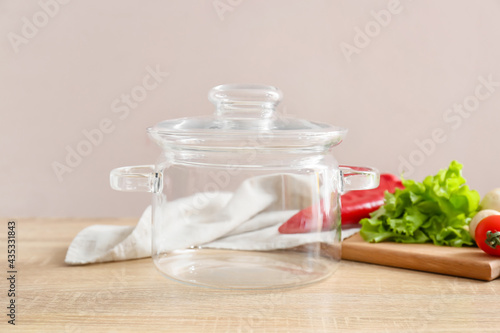 Stylish cooking pot and vegetables on light wooden background