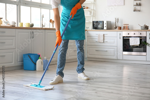 Young man mopping floor in kitchen