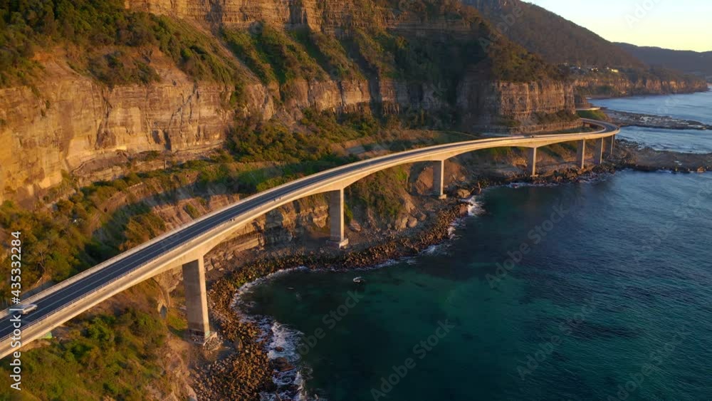 Car Travelling At Sea Cliff Bridge Over Blue Sea In Sunrise At Sydney, NSW, Australia. - aerial
