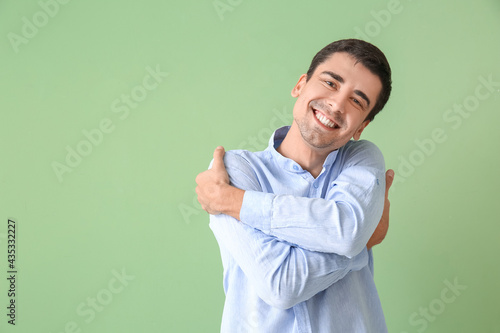 Young man hugging himself on color background photo