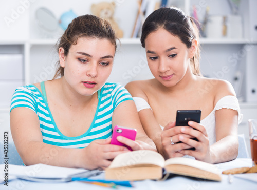 Two girls having fun together at home and watching media in smartphones