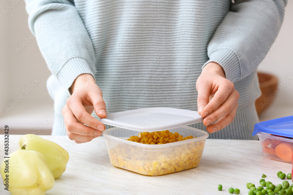 Woman closing plastic container with corn in kitchen, closeup Woman closing plastic container with corn in kitchen, closeup