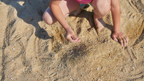 夏の海の海岸で砂遊びしている小学生の女の子の様子