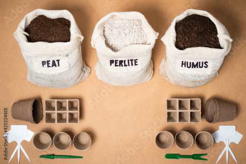 Peat moss, perlite and worm humus in rustic fabric bags for a potting soil mix with peat trays, pots and plant labels on a brown mdf surface with copy space in the middle.