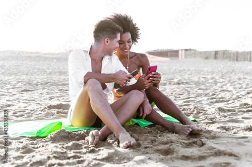 Smiling young couple embracing while looking at smartphone on beach. photo