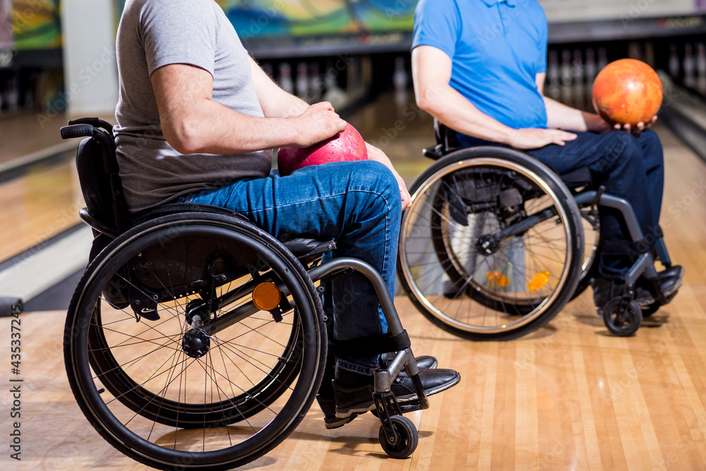 Obraz premium Two young disabled men in wheelchairs playing bowling in the club