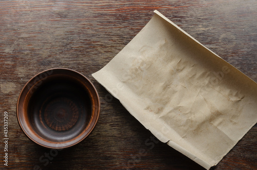 Brown sheet of paper and a clay bowl on a wooden table.