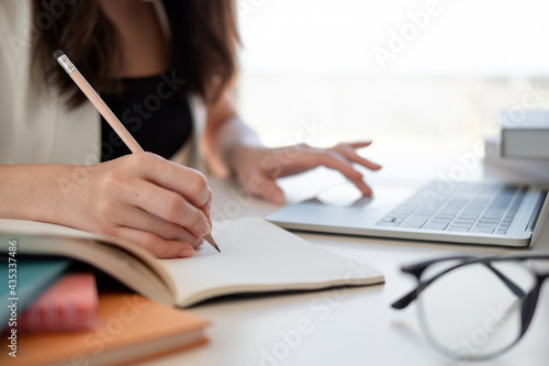 Close up woman's hands with laptop computer, notebook and pen taking notes in business office