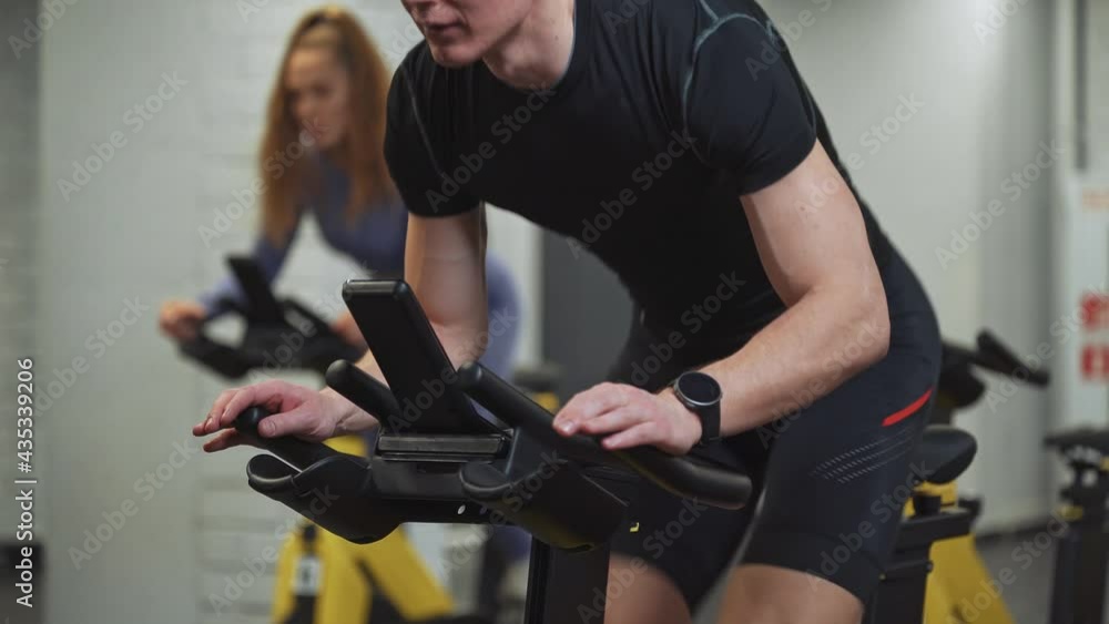 Man and woman training on a spin bikes, performs aerobic endurance training on the simulators in the gym, cycle training. Man and woman training on a spin bikes, performs aerobic endurance training on the simulators in the gym, cycle training.