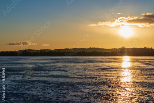 Winter landscape with frozen lake at sunrise or sunset. Lake glistening ice reflect a sun.Forest in the background.