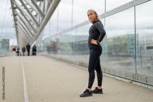 Fit Woman in Black Workout Outfit Standing At Modern Bridge In City