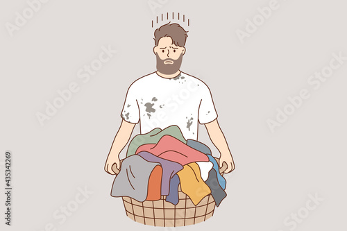 Laundry and washing clothes concept. Young frustrated stressed man cartoon character standing and holding basket with dirty colorful clothes for laundry vector illustration 