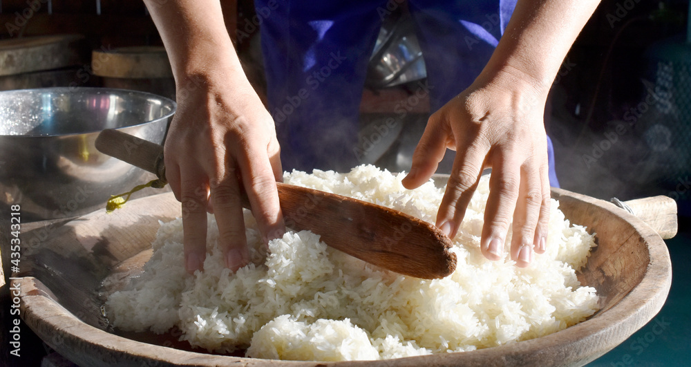 The chef put the hot sticky rice on a wooden tray in the kitchen, using a small long stick to turn the rice down to heat. Sticky rice is a staple food and way of life for people in northern Thailand. 