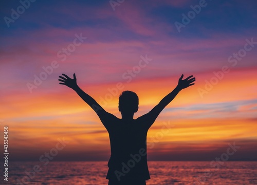 Asian man standing on the beach by the sea at morning sky with sunrise background.