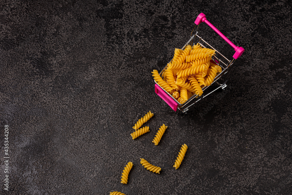 A pile of raw yellow pasta on a dark structural background with space to copy. top view. Macaroni is in the cart