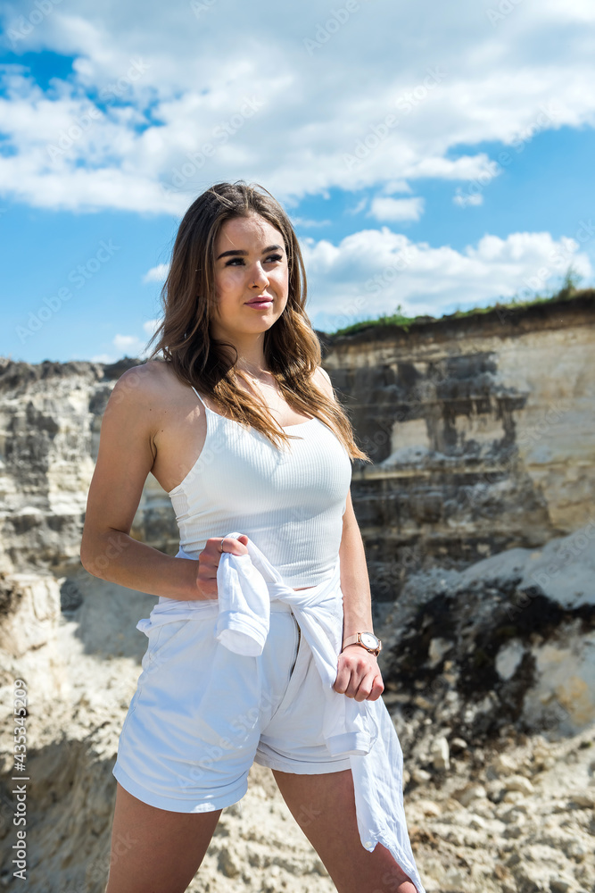 Slim young woman standing on sand near the rock in quarry or canyon