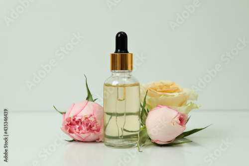 Essential rose oil and roses on white background