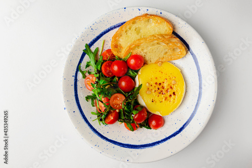 Baked camambert cheese with jam and fresh vegetable salad made from cherry tomatoes and green arugula