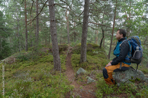 Man sitting with backpack looking at horizon in forest. Relaxing.