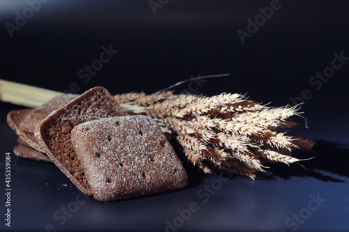 Fresh loaves of bread with wheat and gluten on a black table. Bakery and grocery concept. Fresh, healthy sorts of rye and white loaves food closeup. Fresh homemade bread with cereals.