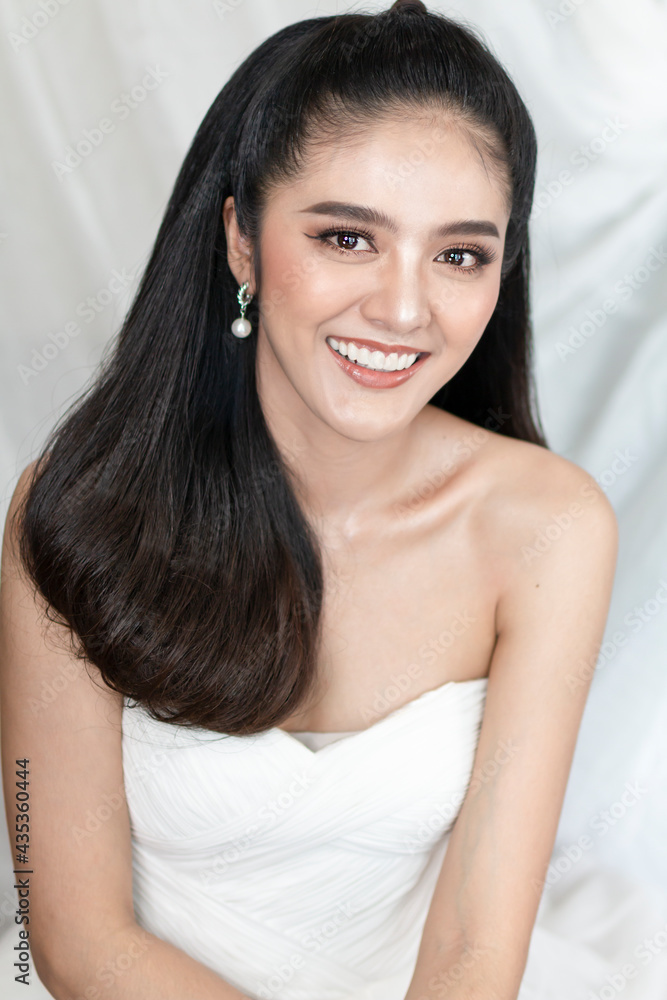 Young Asian teenage girl on white background posing to the camera at home. Portrait of casual Asian woman smiling indoor, wearing beautiful makeup and white wedding dress. Young Asian teenage girl on white background posing to the camera at home. Portrait of casual Asian woman smiling indoor, wearing beautiful makeup and white wedding dress.