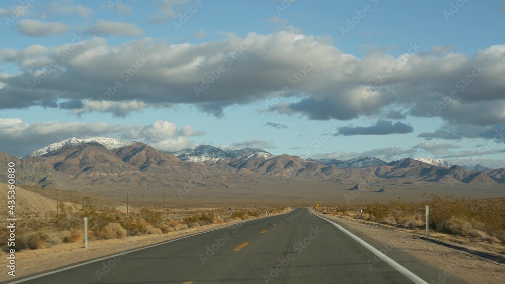 Road trip, driving auto from Death Valley to Las Vegas, Nevada USA. Hitchhiking traveling in America. Highway journey, dramatic atmosphere, clouds, mountain and Mojave desert wilderness. View from car