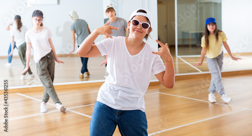 Portrait of emotional teenager girl doing hip hop movements during group class in dance studio © JackF