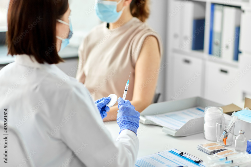 Fototapeta premium health, medicine and pandemic concept - female doctor or nurse wearing protective medical mask and gloves with syringe vaccinating patient at hospital