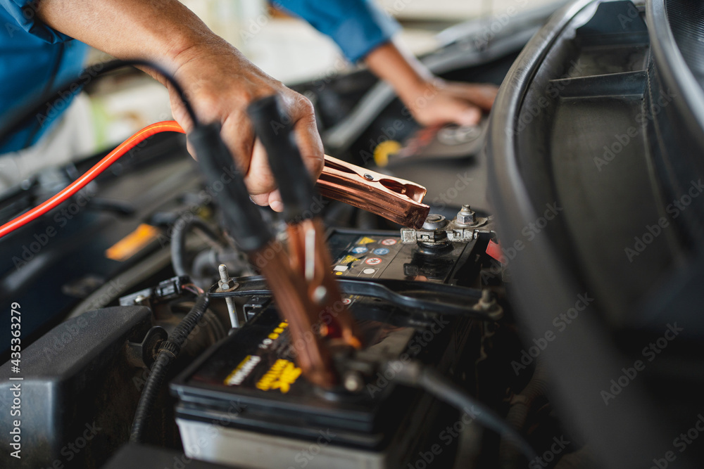 Auto mechanic is charging the battery. He works in a garage. Car repair service and car problems concept. Auto mechanic is charging the battery. He works in a garage. Car repair service and car problems concept.