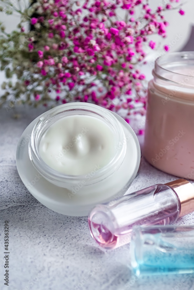 Composition of close-up care products for the skin of the face serum and cream, on a light marble background, pink flowers. Vertical photography Composition of close-up care products for the skin of the face serum and cream, on a light marble background, pink flowers. Vertical photography