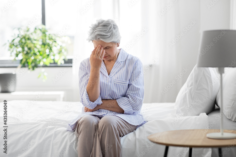 health, old age and people concept - senior woman in pajamas suffering from headache sitting on bed at home bedroom health, old age and people concept - senior woman in pajamas suffering from headache sitting on bed at home bedroom
