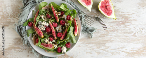 flat lay of white plate with arugula, figs, raspberries and blue cheese salad on light table, space for text