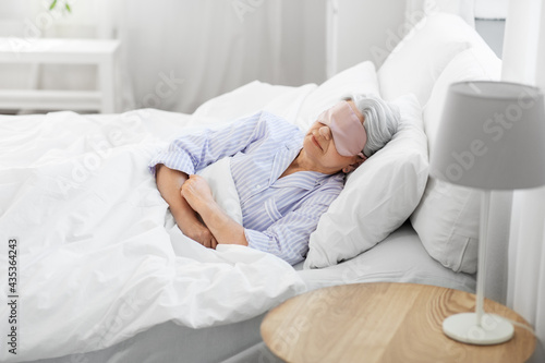 old age and people concept - senior woman with eye mask sleeping in bed at home bedroom