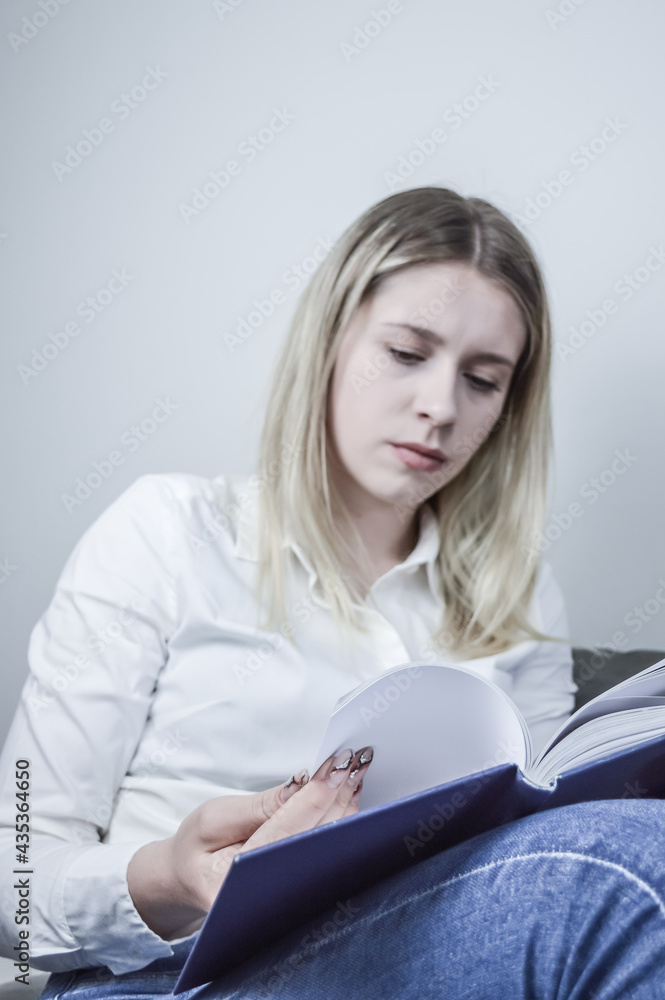 Blue toned portrait of a young blonde long haired woman concentrated in reading a book relaxing Blue toned portrait of a young blonde long haired woman concentrated in reading a book relaxing
