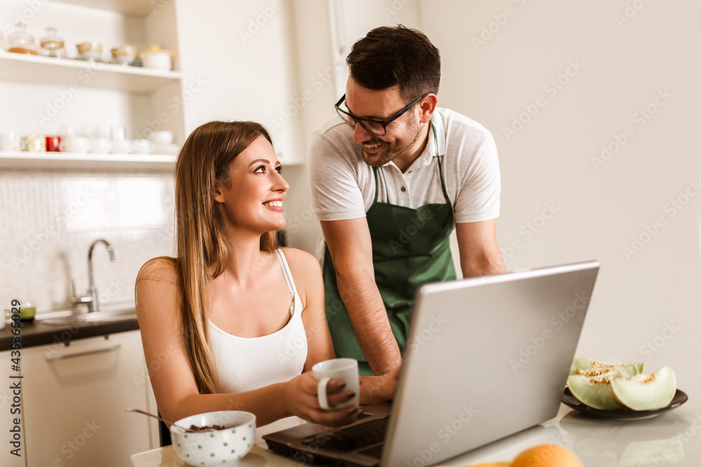 Young couple spending time together at home in the kitchen using laptop. Young couple spending time together at home in the kitchen using laptop.