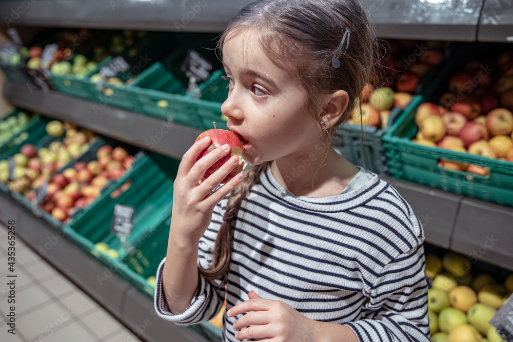 Cute little girl eating an apple in a supermarket.