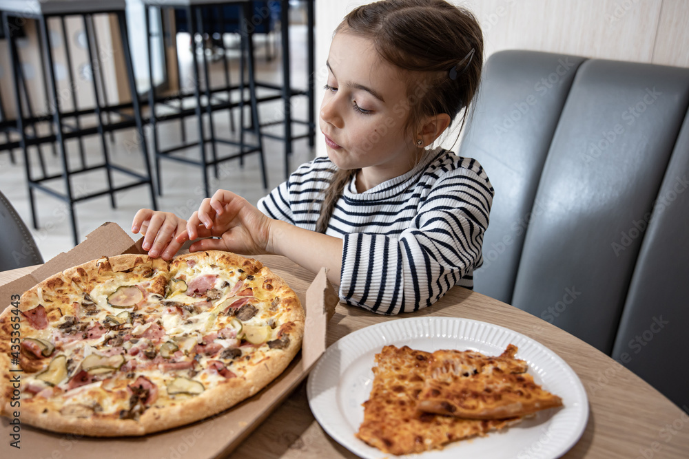 The little girl takes a slice of delicious pizza.