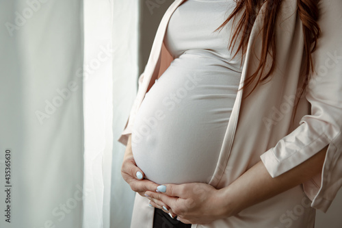 Close up of belly of a pregnant woman standing by the window.