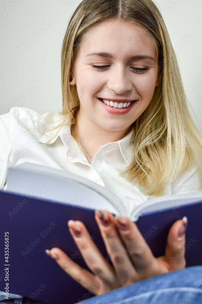 Portrait of a beautiful young blond woman smiling while reading a book Portrait of a beautiful young blond woman smiling while reading a book