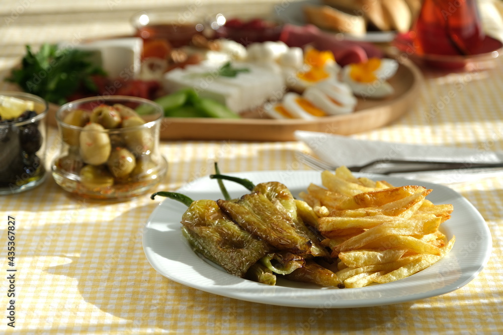 Delicious traditional turkish breakfast on yellow checkered tablecloth.
Tea, olives, eggs, cheeses, cucumbers, tomatoes,
French fries and peppers