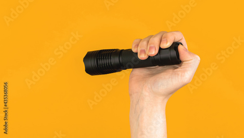 Woman hand holds black EDC flashlight on bright colorful backgroundm equipment outdoor concept photo