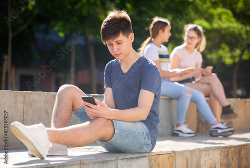 Teen guy plays on smartphone on city street
