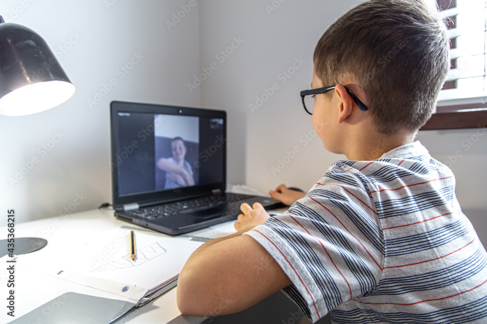 Little boy at the table with a laptop and communicates with a friend remotely. Little boy at the table with a laptop and communicates with a friend remotely.