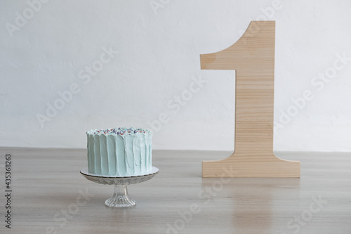 Mint cream cake with sprinkles on a glass stand with big wooden number one on a wooden floor