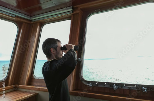 Navigator on the bridge of a large bulk carrier, doing lookout at the horizon with his binoculars.