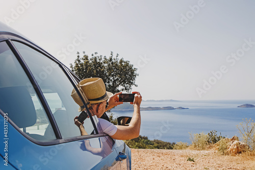 Man taking picture with smarphone from open window of a car