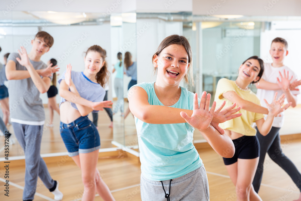 Diligent friendly smiling teenagers learn dance movements in dance class
