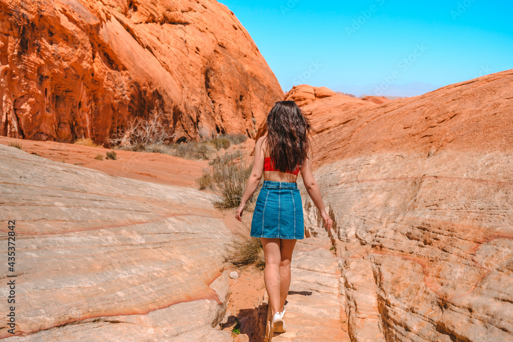 A young woman goes hiking in the Valley of Fire in Nevada, a tourist stands on red wave-shaped stones