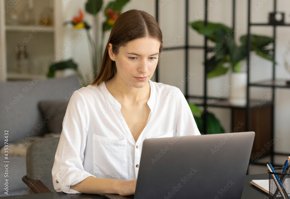 Millennial girl sit at desk at home or office working or studying on laptop in living room Millennial girl sit at desk at home or office working or studying on laptop in living room