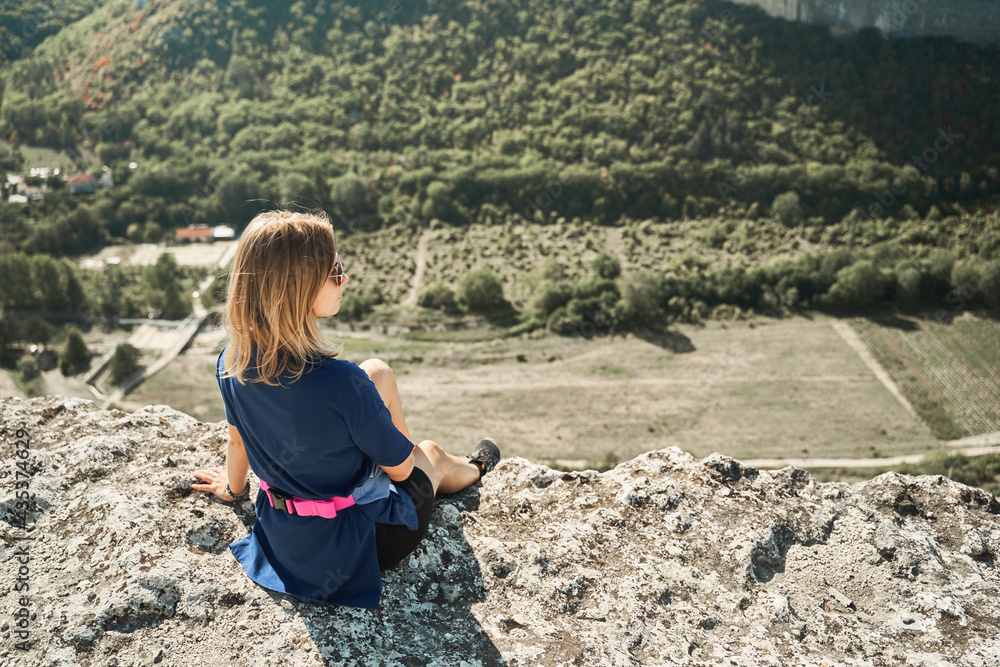 Naklejka premium Young woman sits on a rock, looking at the landscape and enjoying the view and fresh air.